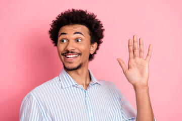 Confident young man gesturing hello with a cheerful expression against vibrant pink background...