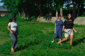 Fototapeta premium The girls jog and playfully run through lush green grass, surrounded by trees and open space.