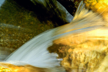 Close-up of clear water cascading over golden-hued rocks at Qing Shan Waterfall, Taiwan, creating a smooth, ethereal effect.