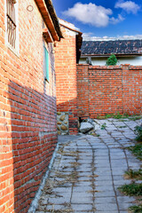 A view of a narrow alleyway with aged red brick walls in Houlong Port, Miaoli County, Taiwan. The ground is paved with stone tiles.