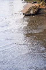A traditional bamboo raft rests on the sandy bank of the Houlong River in Miaoli County, Taiwan. The water shows ripples and reflections, indicating gentle movement.