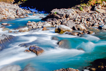 A serene winter stream flows through a rocky forest in Taiwan, with clear blue water and smooth rocks under sunlight.
