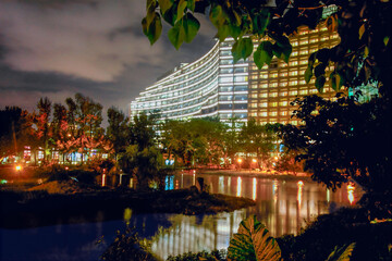 Illuminated modern buildings reflecting on a calm lake at night, surrounded by trees and city lights in Songshan Cultural Park.
