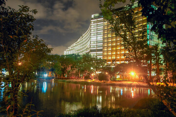 Stunning night view of Songshan Cultural Park in Taipei, with a lit building reflecting on a serene lake surrounded by trees.