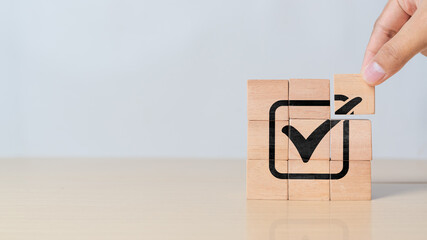 Hand assemble correct tick sign mark on wooden block cube for document approve business project and quality assurance concept