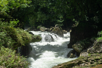 Photograph of a natural river surrounded by vegetation with fast and violent flowing water