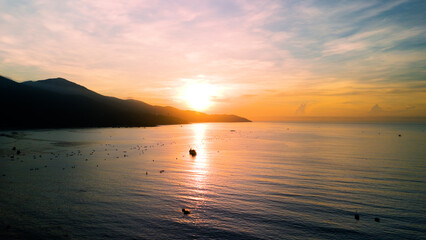 Fishing boats silhouetted against golden sunrise, gliding across tranquil waters of da nang bay, framed by shadowy mountain ridges in vietnamese coastal landscape