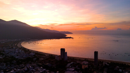 Golden sunlight bathing da nang coastline, fishing vessels anchored near shoreline, modern skyline...