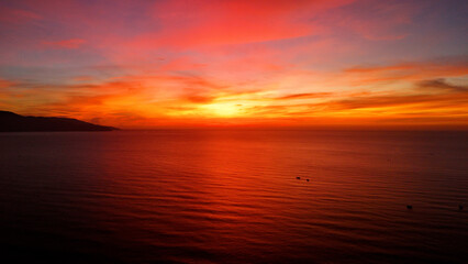 Obraz premium Warm sunlight casting golden rays across serene da nang coastline, illuminating ocean with vibrant orange red horizon