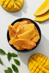 A bowl of dried mango chips with fresh sliced mango