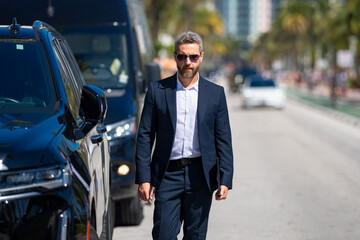 Rich business man near a luxury car. Rich businessman in suit outdoors. Successful rich business man in city. Businessman with a confident look. Success business and rich. Businessman walk on street.