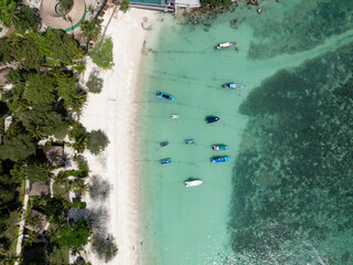 Small wooden boats float on calm, turquoise water near a sandy shore. Thailand, Koh Tao.