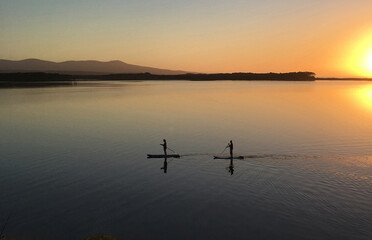 Stand-up paddleboards at sunrise, Mallacoota, Australia. Two people enjoy the serenity of calm...