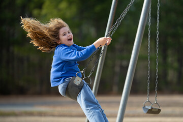 Happy kid swinging outdoors. Laughing child on swing. Joyful kid boy playing at playground. Excited...