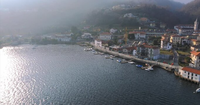 Pella on Lake Orta, sun glinting on wate, waterfront buildings, moored boats, Italy. Aerial drone panoramic view