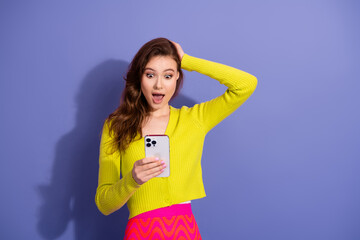 Young cheerful woman in bright fashion outfit excitedly looking at a smartphone against a vibrant...