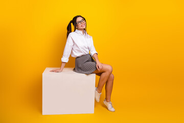 Charming young woman sitting on a styled block against a vibrant yellow background, showcasing...
