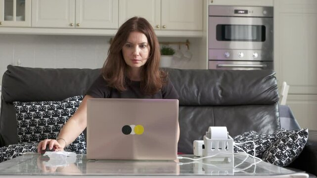 A woman intently connects a label printer to her laptop at a glass table in her modern home.