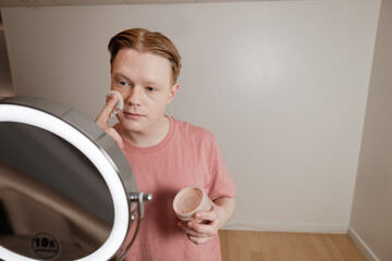 A Medium Shot Of A Man Applying Powder Makeup Mirror Beauty Routine
A young man applies setting...