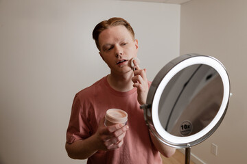 A Medium Shot Of A Man Applying Powder Makeup Mirror Beauty Routine
A young man applies setting...