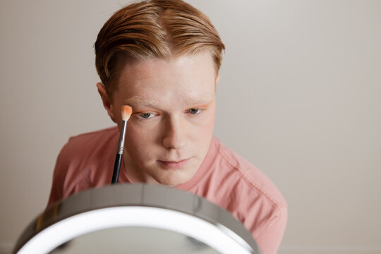 A Close-up of A Young Man Applying Eyeshadow in Front of Mirror
Close-up of a young man applying eyeshadow with a blending brush while looking into a vanity mirror with LED lighting. 