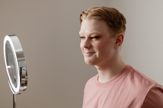 Man Smiling at Mirror with Finished Makeup Look
A young man smiles at his reflection in a vanity mirror after completing his makeup routine. 