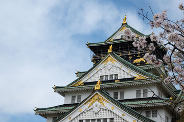 The building exterior of the beautiful acient Osaka Castle framed by pink flowers of cherry trees outdoor at daytime during spring in sakura season in Osaka in Japan.