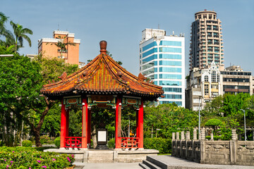 A traditional Chinese pavilion in 228 Peace Memorial Park, Taipei, Taiwan, stands elegantly before a backdrop of modern skyscrapers, reflecting the contrast between cultural heritage and urban