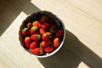 Fresh ripe strawberries with vibrant red hues in a bowl with natural light. Red summer fruit background.