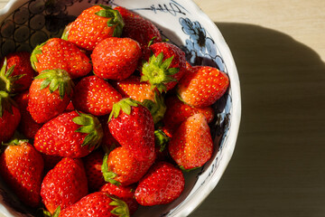 Fresh ripe strawberries with vibrant red hues in a bowl with natural light. Red summer fruit background.