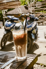 Refreshing iced coffee latte served in a glass with straw outdoor at daytime on the terrace of a restaurant in General Luna on Siargao in the Philippines with blurry background.