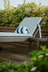 A lounge chair with a soft cushion and a blue and white rolled up towel surrounded by lush greenery outdoor at daytime along the pool of a hotel in Manila during a summer holiday in the Philippines.