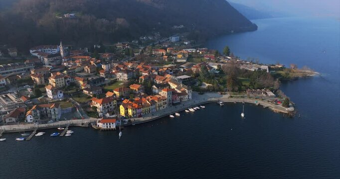 Pella village on Lake Orta, Italy, with buildings and boats along waterfront at dusk. Aerial drone