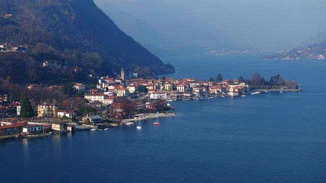 Pella village on shores of Lake Orta, Italy, hazy sky, colorful buildings, boats, ideal for travel, Italian lakes scenery. Aerial drone ascending, copy space