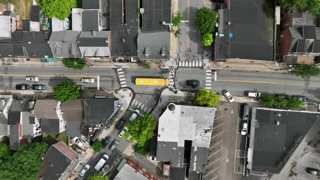 Yellow American school bus on road of town along townhouses and row homes. Sunny day in spring. Traffic scene in the morning. Lancaster, PA, United States. Aerial top down tracking.