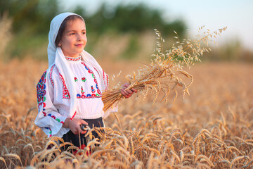 Farmer woman bulgarian little girl in ethnic folklore costume hold golden wheat straws and sickle in harvest field, harvesting and agriculture in Bulgaria