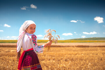 Girl in traditional ethnic folklore costume with Bulgarian embroidery standing on a harvest golden wheat field