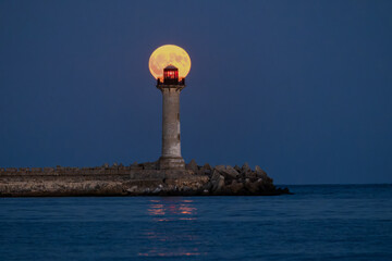 Lighthouse beacon and full moon twilight over sea horizon and moonlight in ripple sea water
