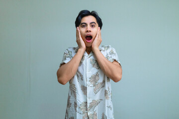 Portrait of a young Asian man in summer clothes with an amazed expression, posing with a surprised hand gesture against a clear background, perfect for promotion or advertisement