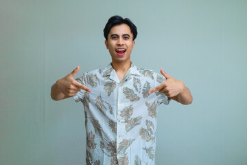 Happy young Asian man in summer outfit smiling and pointing down with both hands, standing against a clear background, perfect for promotions, ads, or social media content
