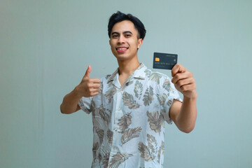 Smiling young Asian man wearing summer clothes holds a product card and gives a thumbs up, perfect for advertisement on a clear background