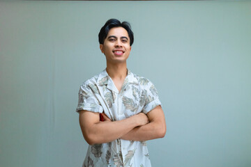 Portrait of a confident young Asian man smiling with arms crossed, wearing casual summer clothes, standing against a clear background, showing positive and relaxed energy