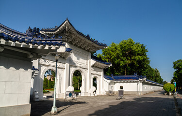 Crisp morning view in Taipei, Taiwan, shows a triple-arched white gate with deep-blue tiled roofs and dragon ornaments marking a side entrance to Liberty Square at Chiang Kai Shek Memorial Hall
