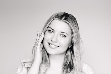 Obraz premium Natural beauty, skincare and cosmetics, smiling blonde woman with blue eyes and radiant face applying moisturiser, light classic elegant monochrome portrait