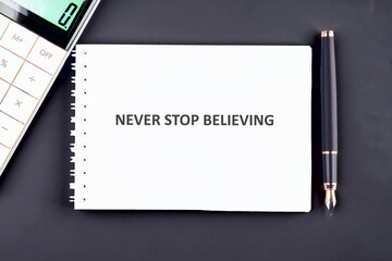 NEVER STOP BELIEVING motivational phrase on a white notebook sheet on a graphite background