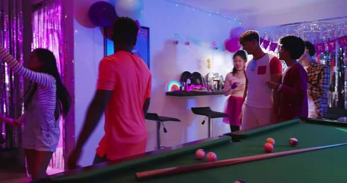 Diverse friends clinking cups after drink offering and dancing by pool table in living room