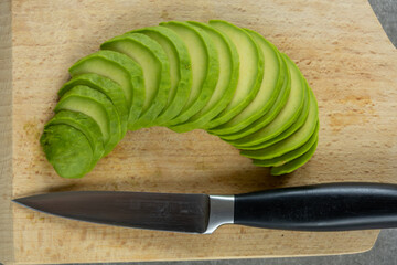 Top-down view of thinly sliced avocado fanned out in a crescent shape on a light wooden cutting board. 