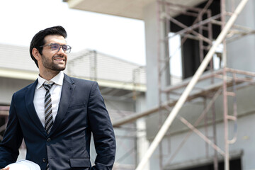 Happy middle aged business man ceo wearing suit standing in site home contruction. Smiling mature businessman professional executive manager looking away thinking working on tech device.