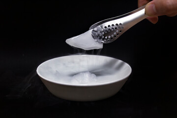 검은색 배경의 금속 집게로 집은 드라이아이스 클로즈업