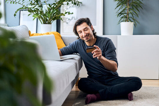 Smiling man looking at credit card while sitting cross-legged at home